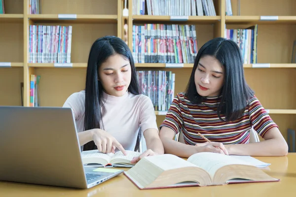 Młody Asian kobieta studia studenckie i bierze notatki z książki w bibliotece. Studentka Uniwersytetu siedzącego przy stole robi zadania w bibliotece kolegium. Student za pomocą laptopa i uczenia się online. — Zdjęcie stockowe