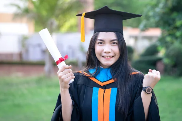 Portrait of happy and excited young Asian female university graduate wears graduation gown and hat celebrates with a degree in the university campus on the commencement day. Education concept.