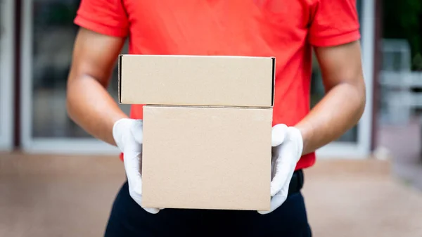 Bir teslimatçının elinde paketler ve kutular var. COVID-19 salgını sırasında online alışveriş siparişi vermek için müşterinin evinin önünde. Teslimatçı paket teslimatı yapıyor..