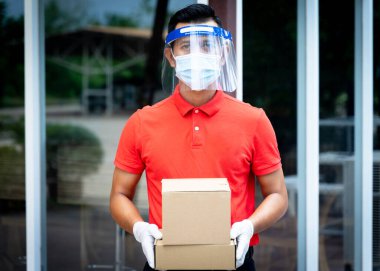 Yüz maskesi ve kalkan giyen teslimatçı adam COVID-19 salgını sırasında müşteri alışverişine paket ve kutu iletiyor. Stok fotoğrafı