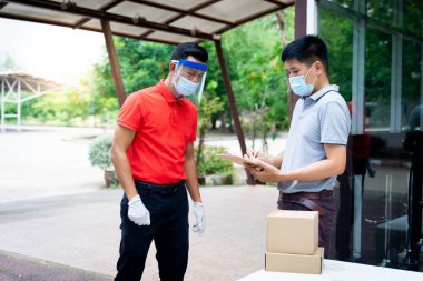 Yüz maskesi ve kalkan giyen teslimatçı adam COVID-19 salgını sırasında müşteri alışverişine paket ve kutu iletiyor. Stok fotoğrafı