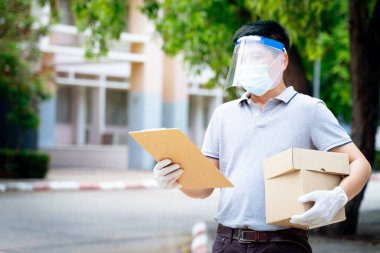 Yüz maskesi ve kalkan giyen teslimatçı adam COVID-19 salgını sırasında müşteri alışverişine paket ve kutu iletiyor. Stok fotoğrafı