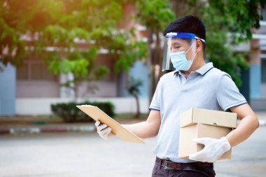 Yüz maskesi ve kalkan giyen teslimatçı adam COVID-19 salgını sırasında müşteri alışverişine paket ve kutu iletiyor. Stok fotoğrafı