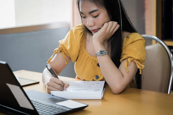 A teenager student studies online via laptop. University student girl watches online classes and writing a syllabus in notebook. Concept of distance study, online learning, webinars. Stock photo.