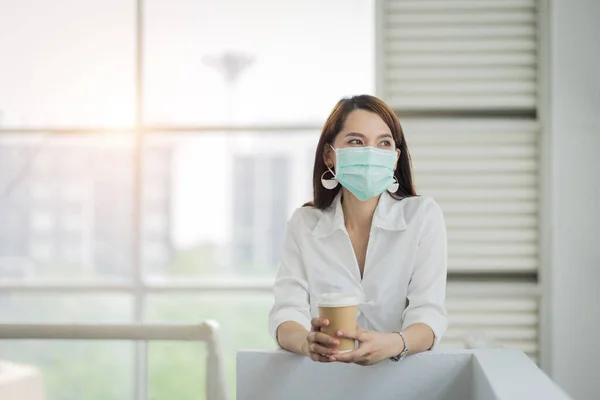 Portrait of a business woman with business suit wearing face mask holding morning coffee cup in company building ready for work. A middle age woman wears face mask to protect COVID-19 pandemic. Business stock photo