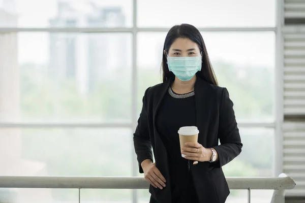 Portrait of a business woman with business suit wearing face mask holding morning coffee cup in company building ready for work. A middle age woman wears face mask to protect COVID-19 pandemic. Business stock photo