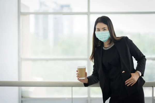 Portrait of a business woman with business suit wearing face mask holding morning coffee cup in company building ready for work. A middle age woman wears face mask to protect COVID-19 pandemic. Business stock photo