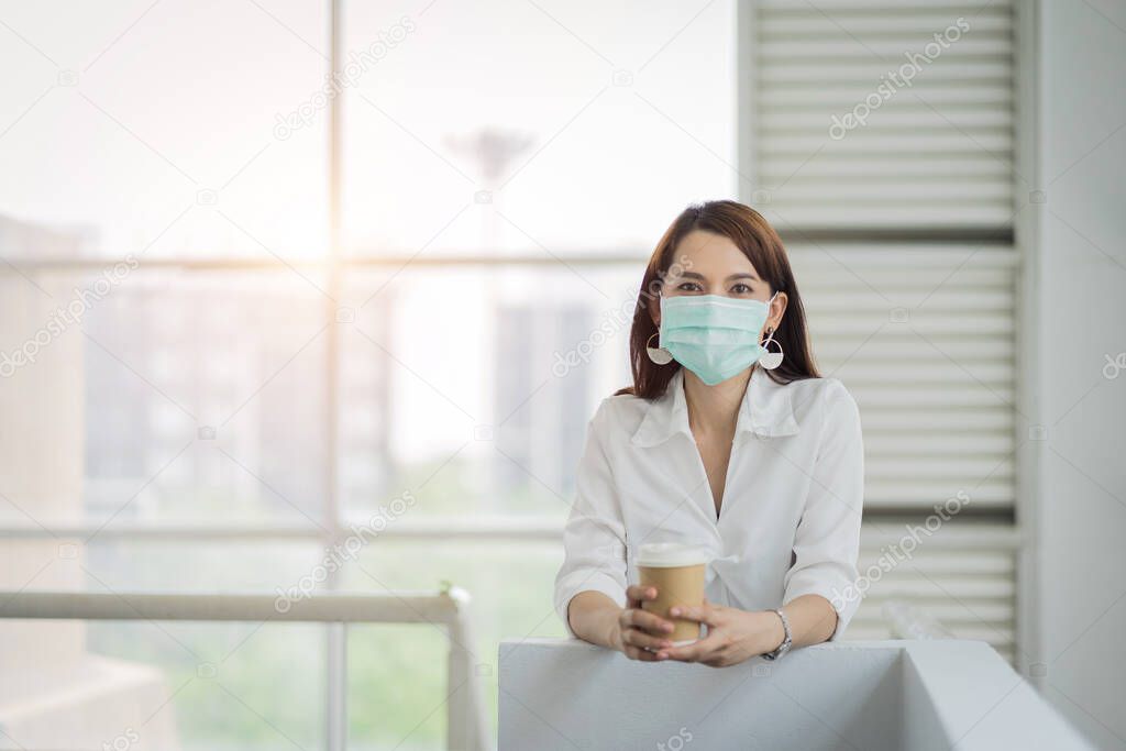 Portrait of a business woman with business suit wearing face mask holding morning coffee cup in company building ready for work. A middle age woman wears face mask to protect COVID-19 pandemic. Business stock photo