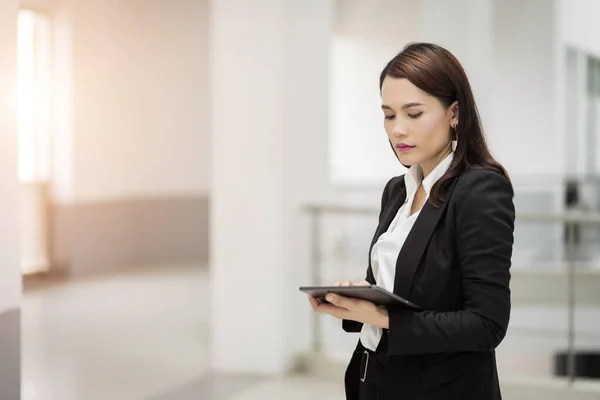 Portrait of a young cheerful businesswoman surfing social network on digital tablet in front of office during break. Asian business woman standing in office building. Stock photo