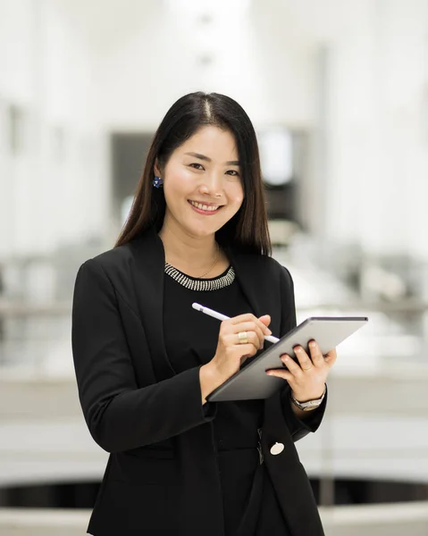 Portrait of a young cheerful businesswoman surfing social network on digital tablet in front of office during break. Asian business woman standing in office building. Business stock photo