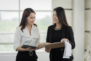 İş elbisesi giymiş iki kadın ofis çalışanı iş binasında tablet ve dosyayla işlerini tartışıyor. İş kadını konuşuyor ve tablet üzerinde duruyor. İş yeri fotoğrafı