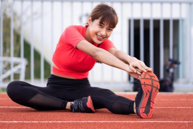 Genç bir kadın koşucunun portresi sabah antrenmandan önce şehir stadyumunda ısınıyor ve esniyor. Sağlıklı ve eğlenceli stok fotoğrafı.