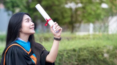Asyalı genç bayan üniversite mezununun mutlu ve heyecanlı portresi mezuniyet elbisesi giyer ve mezuniyet töreninde üniversite kampüsünde dereceyle kutlanır. Eğitim stoku fotoğrafı.