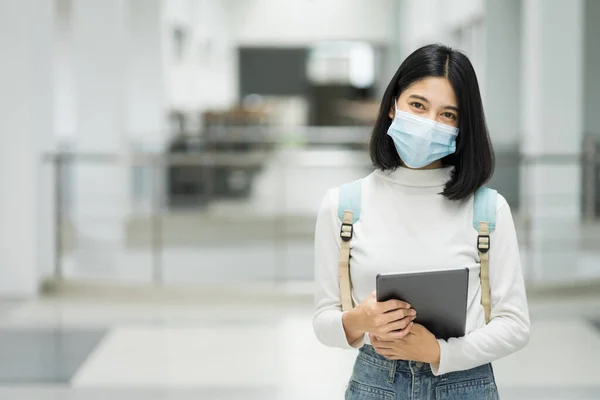 Portrait of a teenage college student wearing medical protective face mask with school backpack to protect from influenza virus, COVID-19 pandemic in college building. Back to school. Education stock photo.