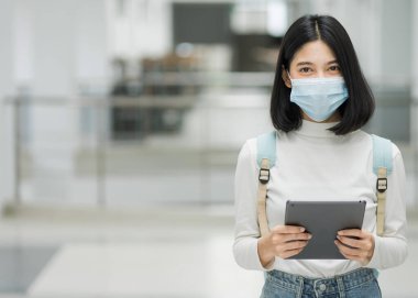 Üniversite binasında grip virüsünden korunmak için okul çantasıyla tıbbi koruyucu maske takan genç bir üniversite öğrencisinin portresi. Okula dönelim. Eğitim stoku fotoğrafı.