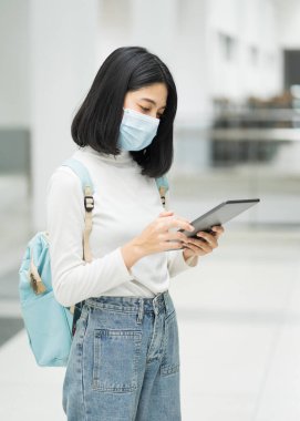 Üniversite binasında grip virüsünden korunmak için okul çantasıyla tıbbi koruyucu maske takan genç bir üniversite öğrencisinin portresi. Okula dönelim. Eğitim stoku fotoğrafı.