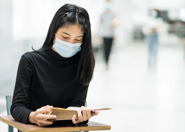 Portrait of a teenager college student wears face mask while reading book in college campus to prevent COVID-19 pandemic. Education stock photo.