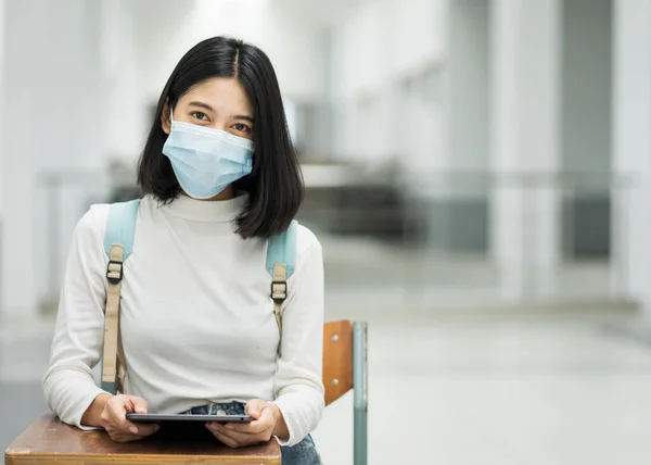 Portrait of a teenage college student wearing medical protective face mask with school backpack to protect from influenza virus, COVID-19 pandemic in college building. Back to school. Education stock photo.