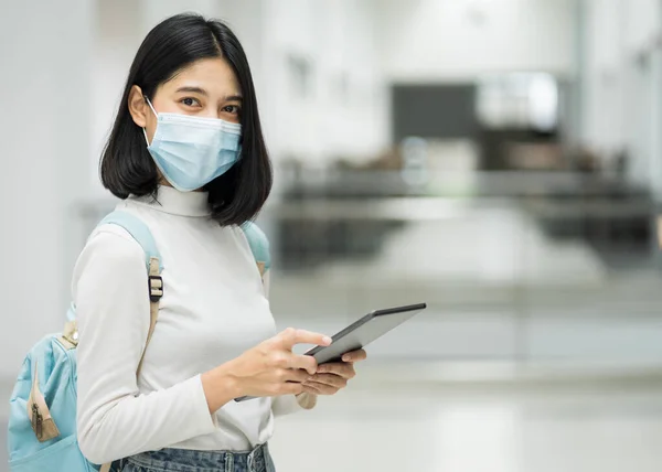 Portrait of a teenage college student wearing medical protective face mask with school backpack to protect from influenza virus, COVID-19 pandemic in college building. Back to school. Education stock photo.