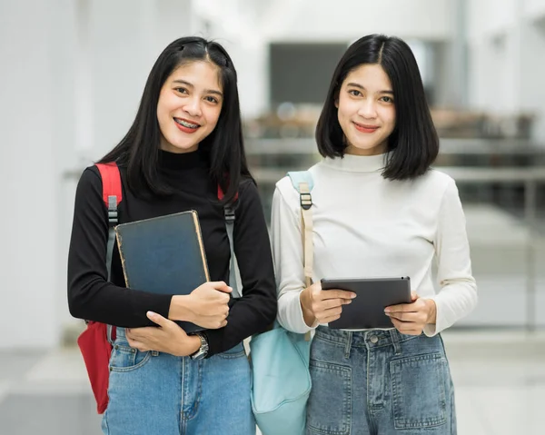 Teenage college friend students walking and chatting in college campus while having break after class. Two happy students walking and talking each other in a campus. Education stock photo.