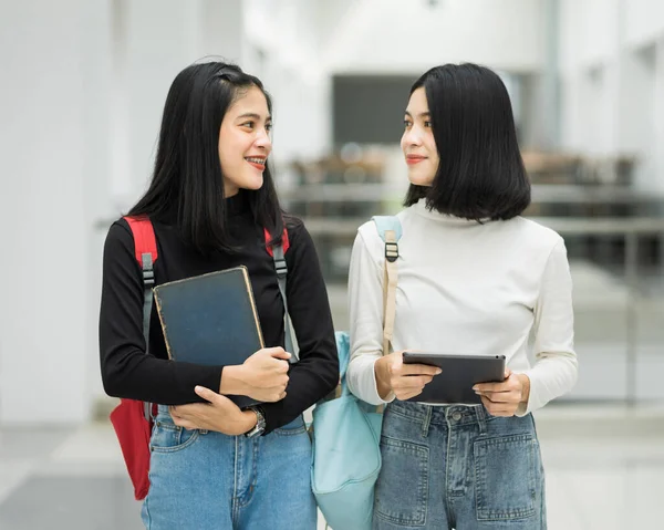 Teenage college friend students walking and chatting in college campus while having break after class. Two happy students walking and talking each other in a campus. Education stock photo.