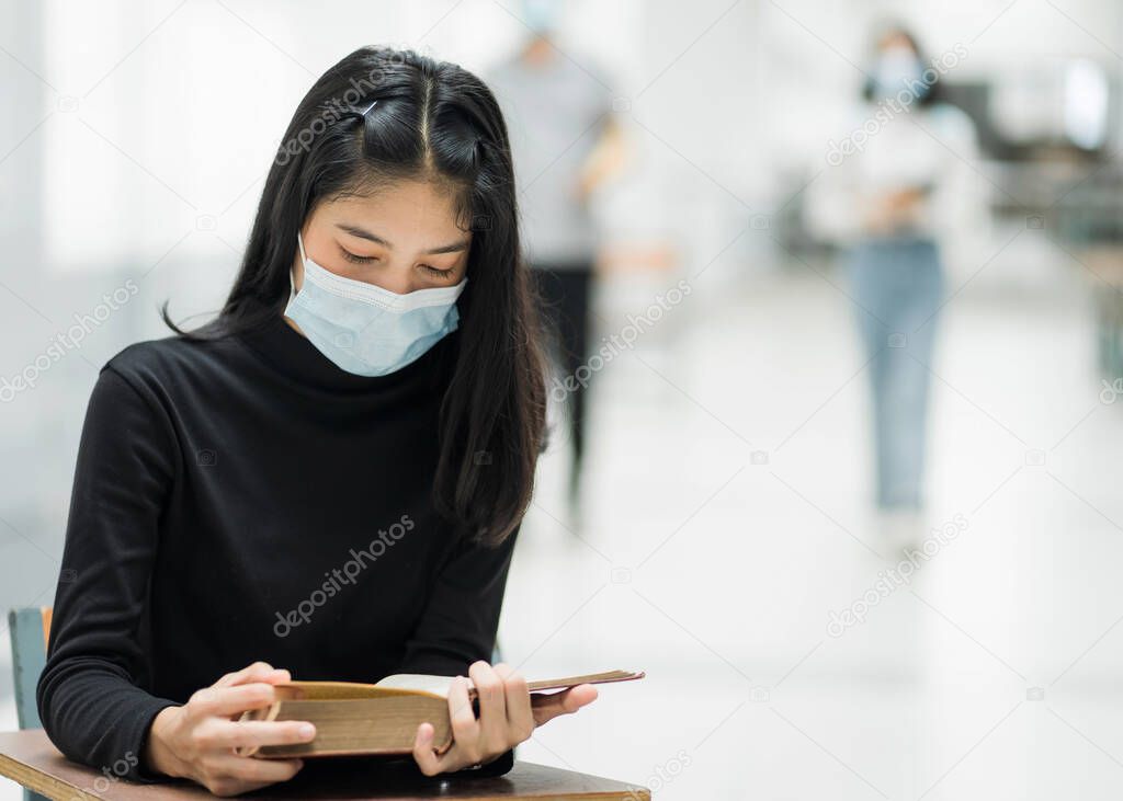 Portrait of a teenager college student wears face mask while reading book in college campus to prevent COVID-19 pandemic. Education stock photo.