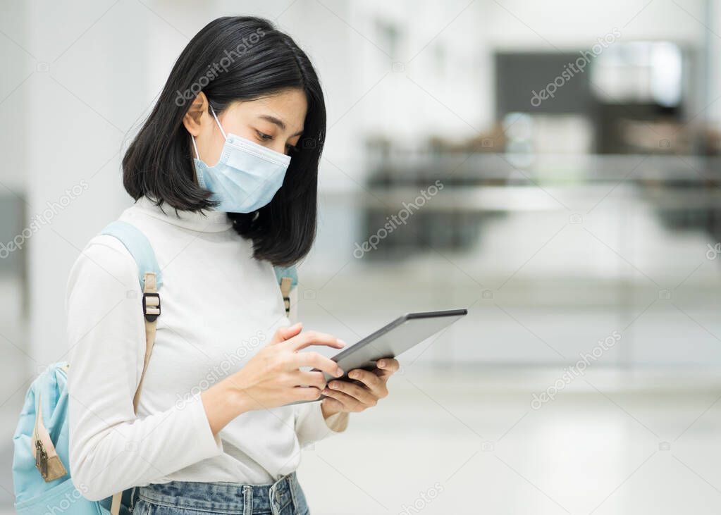 Portrait of a teenage college student wearing medical protective face mask with school backpack to protect from influenza virus, COVID-19 pandemic in college building. Back to school. Education stock photo.
