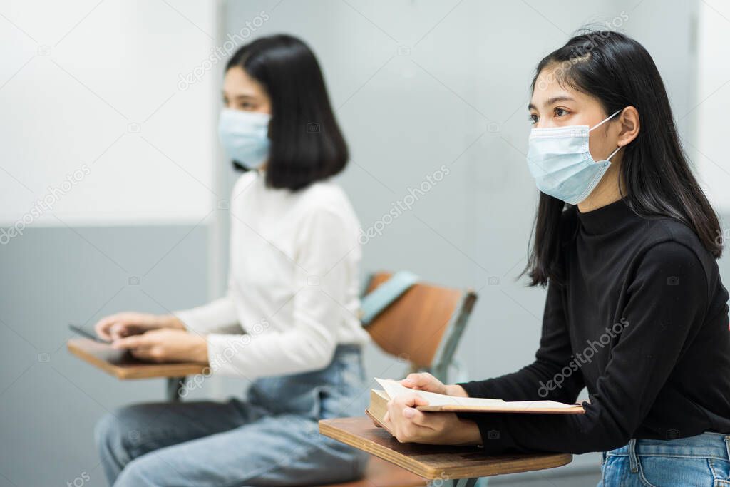 Female teenager college students wears face mask and keep distance while studying in classroom and college campus to prevent COVID-19 pandemic. Education stock photo.
