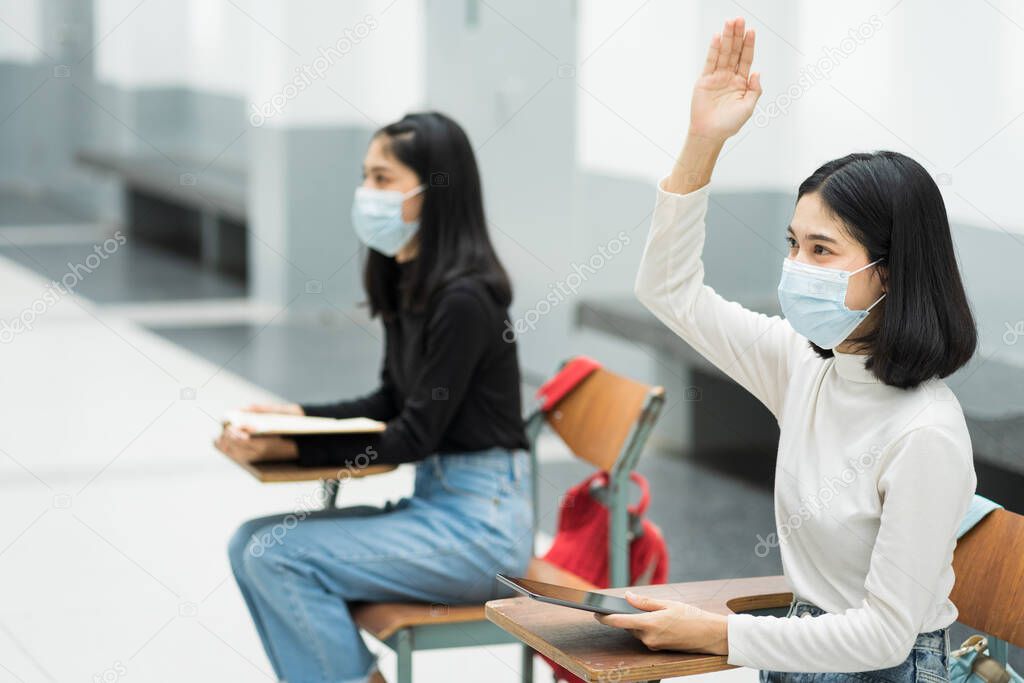 Teenage college students sitting in the class and raising hand up to participate ask question during lecture. High school student raises hand and asks lecturer a question. Education stock photo.