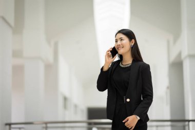 Genç Asyalı bir iş kadınının portresi cep telefonuyla konuşuyor ve iş binasında bir fincan kahve tutuyor. Güzel bir kızın resmi. Günlük süitte, telefon ve bir fincan kahveyle. Stok fotoğrafı