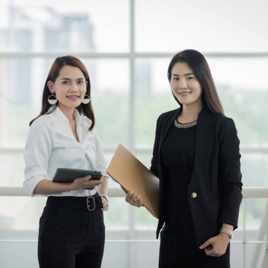 İş elbisesi giymiş iki kadın ofis çalışanı iş binasında tablet ve dosyayla işlerini tartışıyor. İş kadını konuşuyor ve tablet üzerinde duruyor. İş yeri fotoğrafı