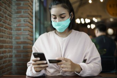 Kafede kredi kartıyla ödeme yaparken yüz maskesi takan Asyalı genç bir kadının portresi. Genç bayan, kafede COVID-19 'u önlemek için yüz maskesi takıyor. Stok fotoğrafı.