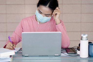 Coronavirus ya da COVID-19 salgını sırasında evde dizüstü bilgisayarda çalışan yüz maskeli genç Asyalı iş kadını ev konseptinden çalışıyor. Stok fotoğrafı