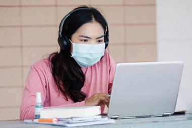 Coronavirus ya da COVID-19 salgını sırasında evde dizüstü bilgisayarda çalışan maskeli genç bir kadın evde online çalışan bir ault öğrencisidir. Stok fotoğrafı