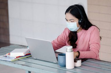 Coronavirus ya da COVID-19 salgını sırasında evde dizüstü bilgisayarda çalışan maskeli genç bir kadın evde online çalışan bir ault öğrencisidir. Stok fotoğrafı