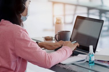 Coronavirus ya da COVID-19 salgını sırasında evde dizüstü bilgisayarda çalışan maskeli genç bir kadın evde online çalışan bir ault öğrencisidir. Stok fotoğrafı