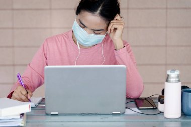 Coronavirus ya da COVID-19 salgını sırasında evde dizüstü bilgisayarda çalışan maskeli genç bir kadın evde online çalışan bir ault öğrencisidir. Stok fotoğrafı