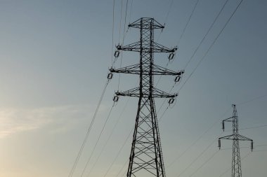Günbatımında açık gökyüzünde elektrik kabloları olan yüksek voltajlı güç iletim kuleleri, modern enerji altyapısı ve elektrik dağıtımının sembolü. Teknoloji, endüstri ve sürdürülebilirlik