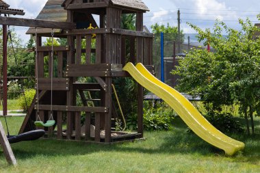 Dayanıklı sarı kaydırak ve bahçe bahçesinde güneşli bir yaz günü spor malzemesi olarak tasarlanan salıncaklı ahşap oyun parkı. Fiziksel aktivite, sağlıklı yaşam tarzı ve çocukların egzersizi.