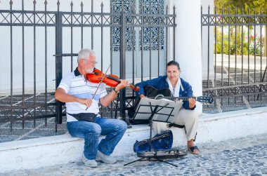 GREECE, SANTORINI ISLAND - JULY 17, 2014: Street musicians playing music for people on streets. clipart