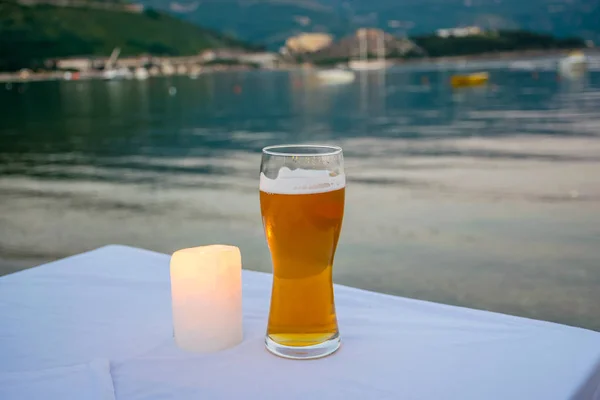glass of delicious light beer on restaurant table near sea.