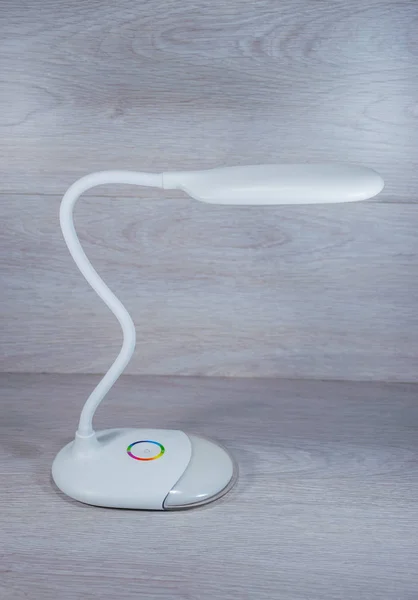 White flexible desktop energy-saving LED lamp on wooden background