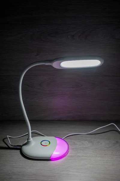 White flexible desktop energy-saving LED lamp on wooden background