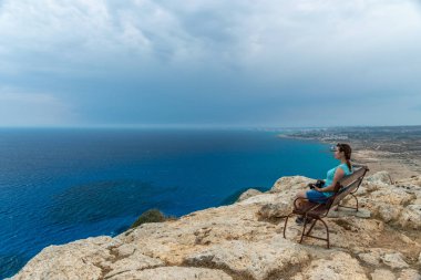 Ahşap bir bankta, genç bir kız denizden esinti sahiptir.