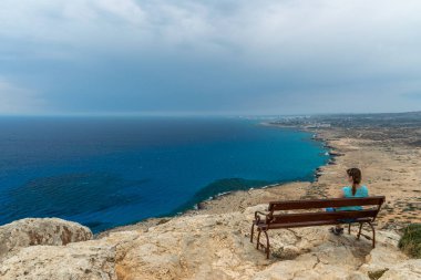 Ahşap bir bankta, genç bir kız denizden esinti sahiptir.