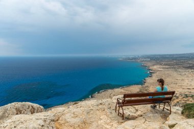 Ahşap bir bankta, genç bir kız denizden esinti sahiptir.