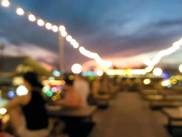 Blurred customers dining at outdoor restaurant with colorful bokeh light in the evening