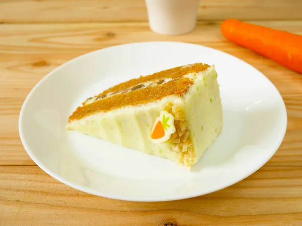 Slice of carrot cake with cream cheese frosting and walnuts on a white plate