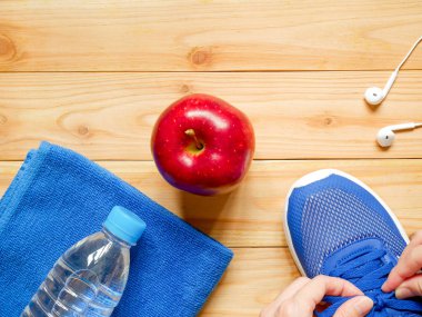 Ayakkabı bağcığı bağlama eller. Egzersiz ve fitness ekipmanları. Bir şişe su, kulaklık, Kırmızı elma ve havlu kopya alanı ile spor salonunda ahşap arka plan üzerinde. Üstten Görünüm. Sağlık kavramı