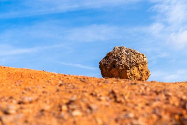 Terk edilmiş bir boksit madeninde parlak turuncu renkte, arka planda mavi gökyüzü olan aşınmış boksit kayası.